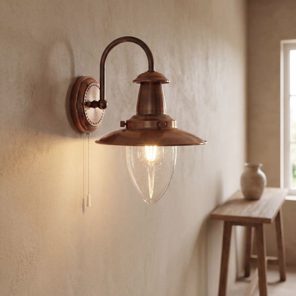 Wandleuchte aus Kupfer im Vintage-Stil mit Glasschirm und Zugschalter an strukturierter Wand, heller Raum mit hölzernem Beistelltisch.