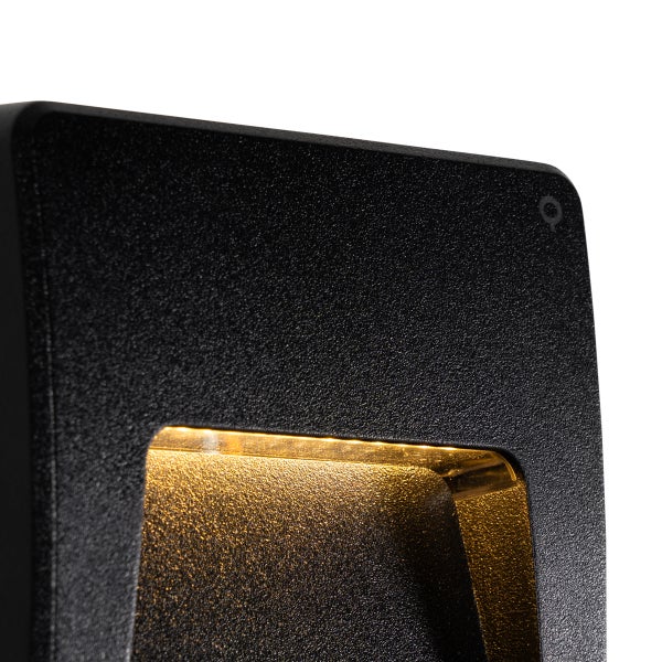 Schwarze Außenwandleuchte mit strukturierter Oberfläche und warmem Lichtstrahl.