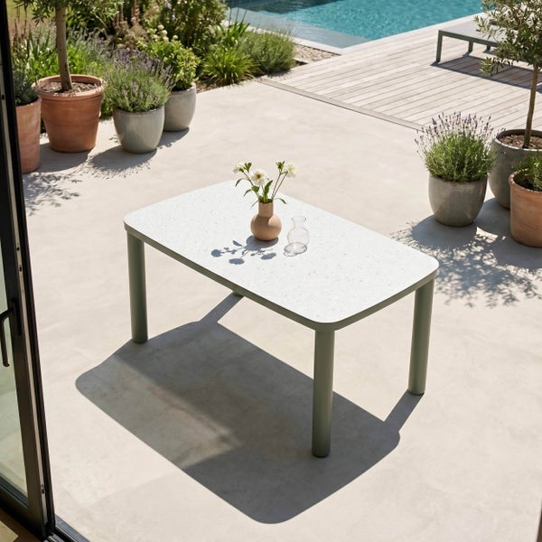 Moderner rechteckiger Gartentisch mit heller Platte und grünen Beinen auf einer hellen Terrasse mit Pflanzen und Pool.