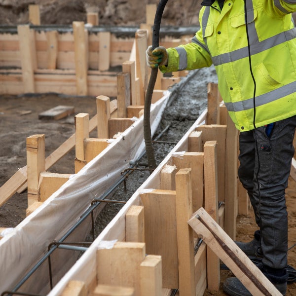Betonieren einer Fundamentform mit Armierungseisen durch eine Person mit einem Schlauch
