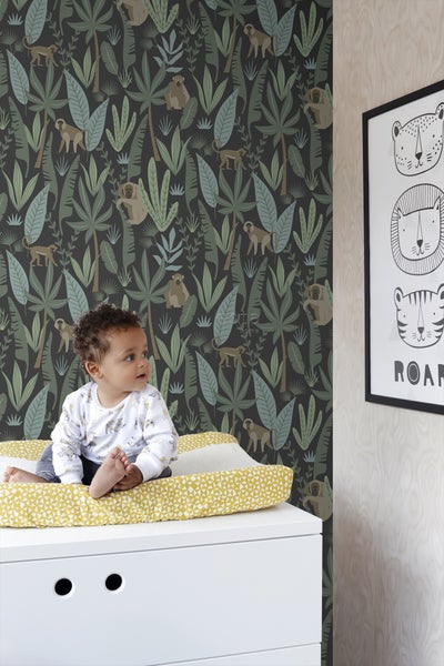 Baby auf einer Wickelauflage vor einer Dschungeltapete mit Affen und Pflanzen