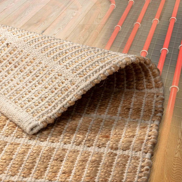 Handgewebter Teppich aus Naturfasern auf Holzboden, geeignet für Fußbodenheizung mit sichtbaren Heizrohren.