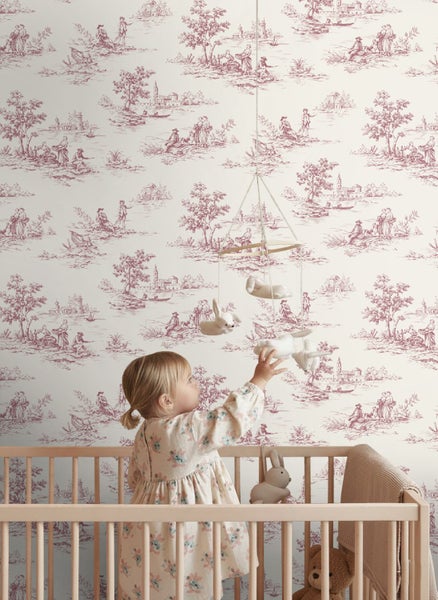 Vliestapete im Toile-de-Jouy-Stil mit ländlichen Motiven in einem hellen Kinderzimmer mit Babybett aus Holz.