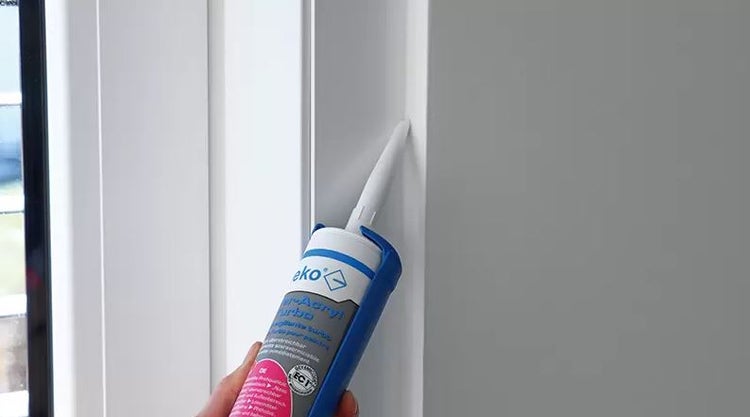 Anwendung von Acryl-Dichtstoff aus einer Kartusche in eine Fuge zwischen Fensterrahmen und Wand.