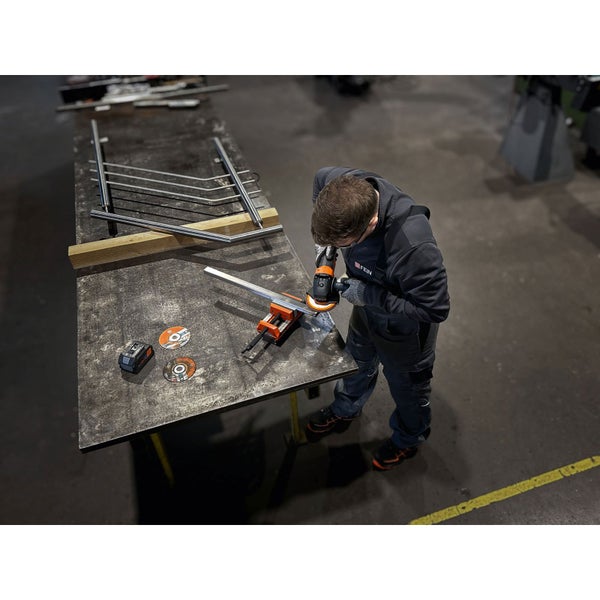 Ein Mann schleift ein Metallstück mit einem Winkelschleifer, das in einem Schraubstock fixiert ist.