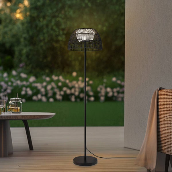 Außenstehleuchte mit geflochtenem Schirm auf einer Holzterrasse, Garten im Hintergrund.