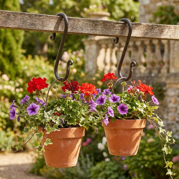 Zwei Tontöpfe mit Blumen hängen an S Haken an einem Holzbalken im Garten