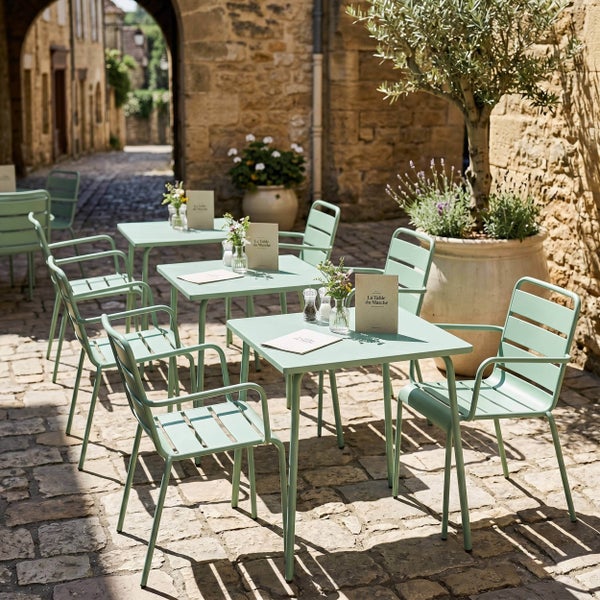 Gartenmöbel Set aus Metall mit quadratischen Bistrotischen und Armlehnstühlen auf einer gepflasterten Terrasse.
