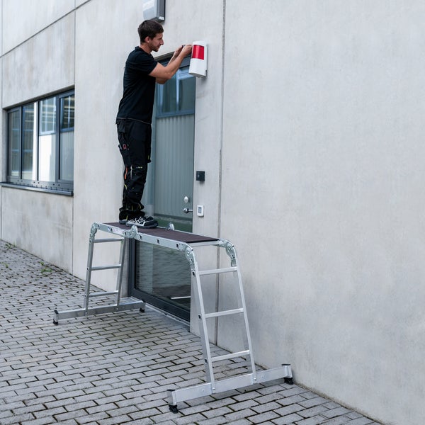 Handwerker auf einer Aluminium Arbeitsplattform bei der Installation einer Lampe an einer Fassade.