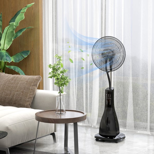 Schwarzer Standventilator mit Sprühnebelfunktion in einem hellen Wohnzimmer neben einem Sofa und Fenster.