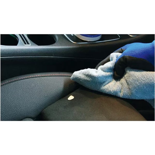 Eine Hand mit Handschuh reinigt einen Autositz mit einem Mikrofasertuch und Reinigungsmittel.