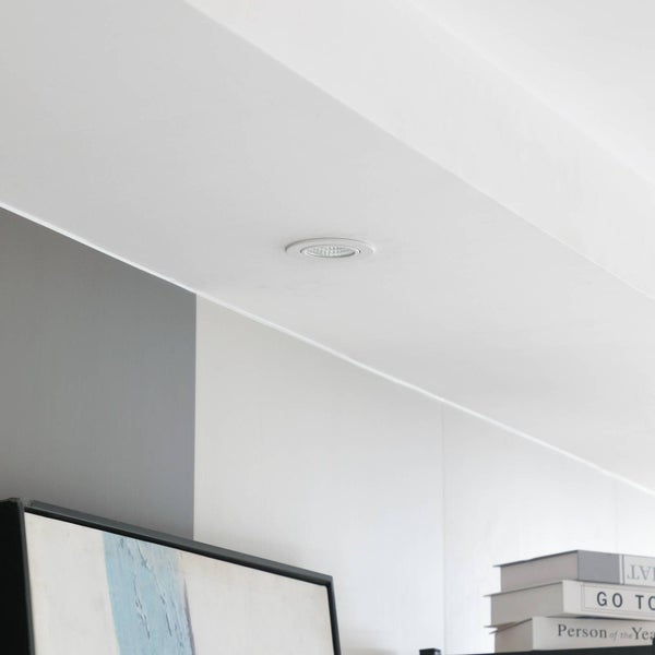 Runder LED-Einbaustrahler in einer weißen Decke über einem Regal montiert.