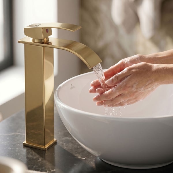Goldene Waschtischarmatur mit hohem Auslauf, Hände waschen in einem weißen Aufsatzwaschbecken aus Keramik.