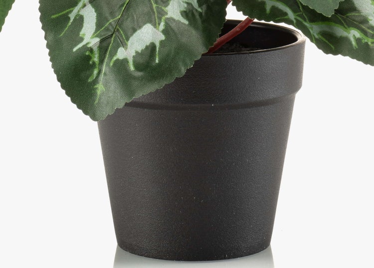 Nahaufnahme eines schwarzen Kunststoff-Blumentopfs mit grün gemusterten künstlichen Blättern.