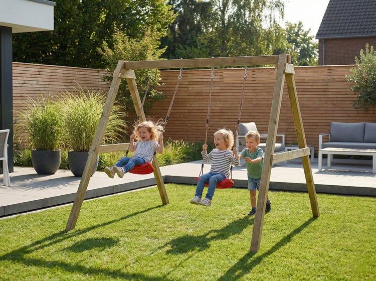 Kinderschaukel aus Holz im Garten mit zwei Schaukelsitzen und drei spielenden Kindern auf einer Rasenfläche vor einem Holzzaun.