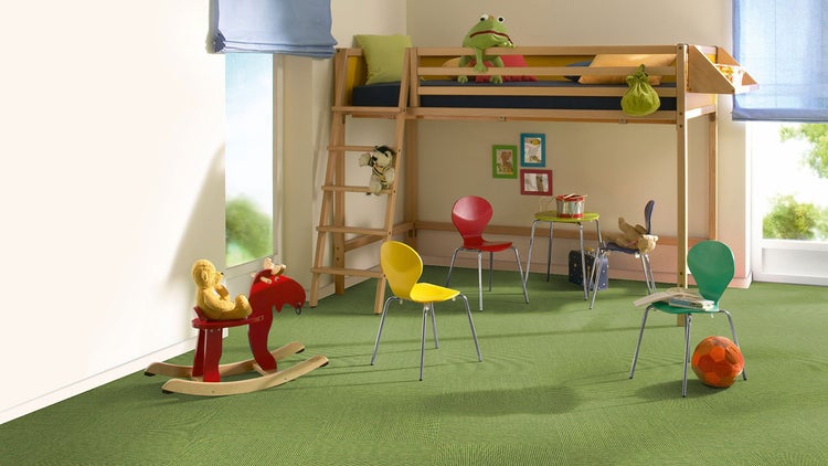 Grüne Teppichfliesen in einem hellen Kinderzimmer mit Hochbett aus Holz und bunten Stühlen.
