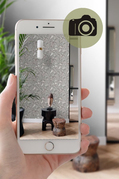 Aufnahme eines Raumes mit gemusterter Tapete, Pflanzen und dekorativen Elementen, aufgenommen mit einem Mobiltelefon.