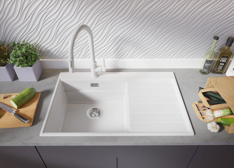 Spüle aus Keramik mit Abtropffläche, Armatur und Lebensmitteln in einer hellen Küche.