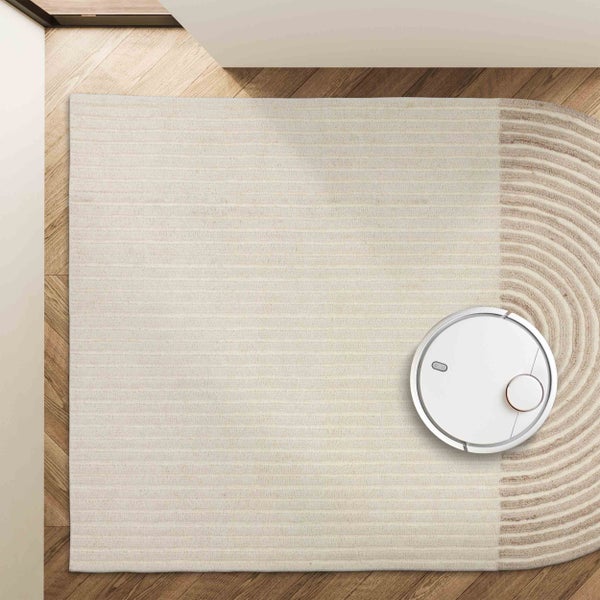 Weißer Saugroboter auf einem gestreiften Teppich und Holzboden in der Draufsicht.