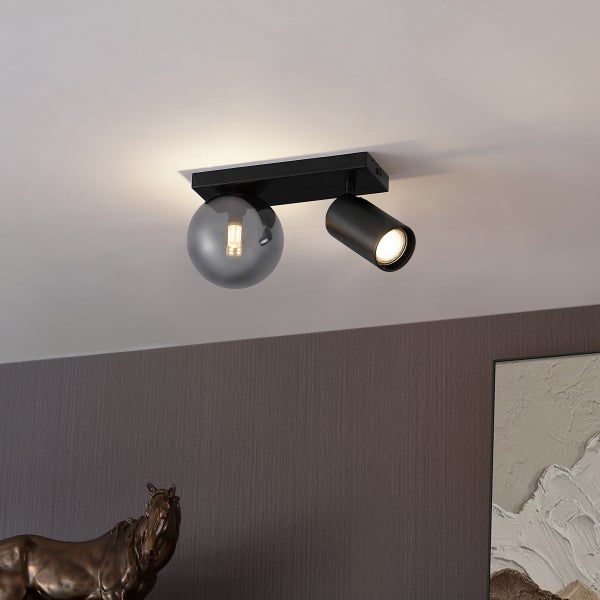 Moderne schwarze Deckenleuchte mit zwei Lichtquellen, einer Rauchglaskugel und einem verstellbaren Spot, an der Decke montiert.