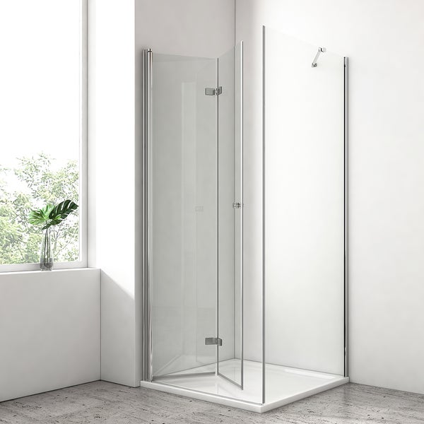 Eckdusche mit Falttüren aus Klarglas und verchromten Profilen auf weißer Duschwanne in hellem Badezimmer mit Fenster.