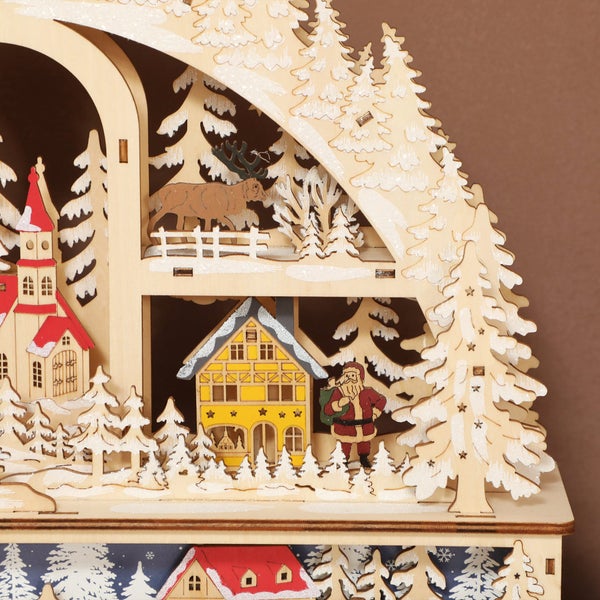 Detail einer hölzernen Weihnachtsdekoration mit Haus, Weihnachtsmann, Rentier und verschneiten Tannen.