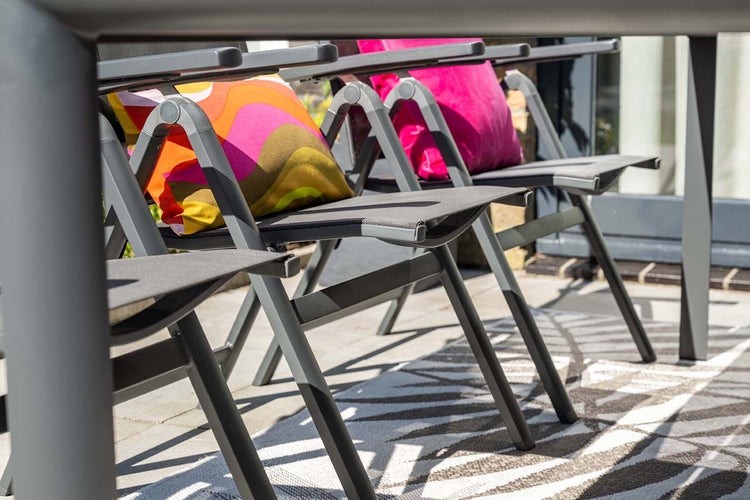 Graue Gartenstühle aus Metall mit Textilgewebe und bunten Kissen auf einem gemusterten Außenteppich auf einer Terrasse.