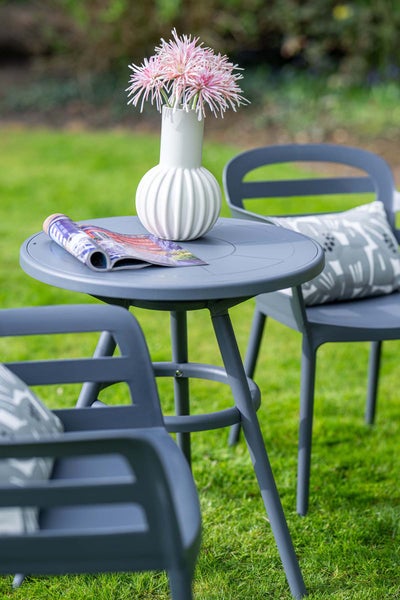 Moderne graue Garten-Sitzgruppe aus Kunststoff mit rundem Tisch und zwei Stühlen auf einer Rasenfläche. Tisch mit Vase und Zeitschrift.