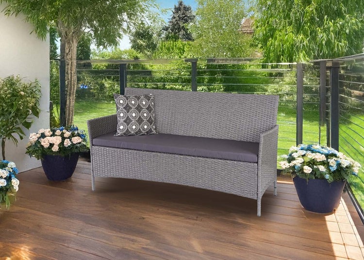 Gartenbank aus grauem Polyrattan mit Sitzkissen auf einer Holzterrasse mit Blumenkübeln vor einer Glasbrüstung und hellem Garten.