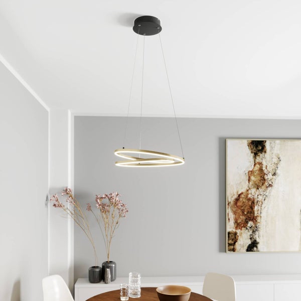 Moderne LED-Pendelleuchte mit zwei ineinandergreifenden Ringen in Gold-Optik über einem Esstisch in einem hellen, minimalistischen Raum.