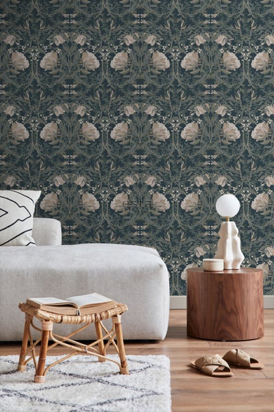 Ein Zimmer mit einem Sofa, einem Holzhocker mit einem Buch, einem Holztisch mit einer Lampe und einer floralen Tapete.