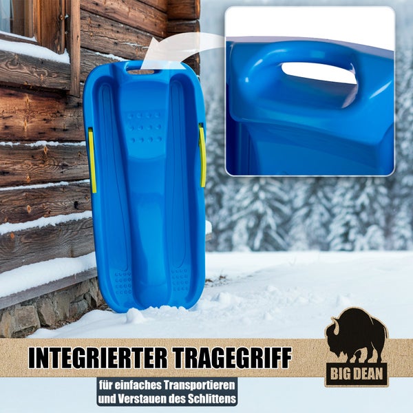 Kind fährt auf einem Kunststoffschlitten mit seitlichen Bremshebeln im Schnee, Detailansicht der Bremsen und Big Dean Logo.