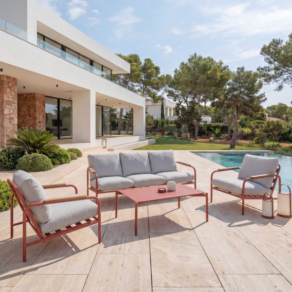 Modernes Garten-Lounge-Set aus Metall mit Dreisitzer-Sofa, Sesseln und Tisch auf einer hellen Steinterrasse am Pool neben einer modernen Villa.