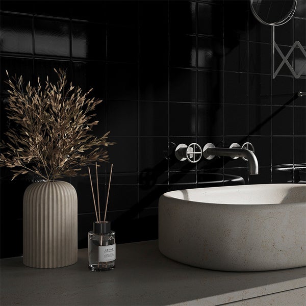 Modernes Badezimmer mit Steinwaschbecken, wandmontierter Armatur, gerippter Vase mit Zweigen und Raumduft vor einer gefliesten Wand.