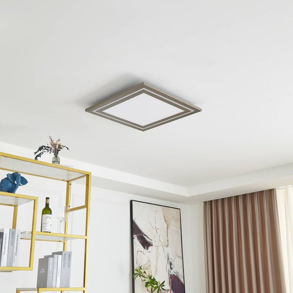 Moderne quadratische LED-Deckenleuchte in einem hellen Zimmer mit weißer Decke, goldenem Regal und abstrakter Wandkunst.