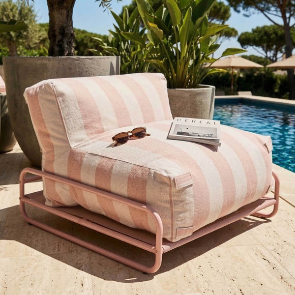 Gestreifter Outdoor-Loungesessel auf Metallgestell am Pool, umgeben von großen Pflanzengefäßen in sonniger Atmosphäre.