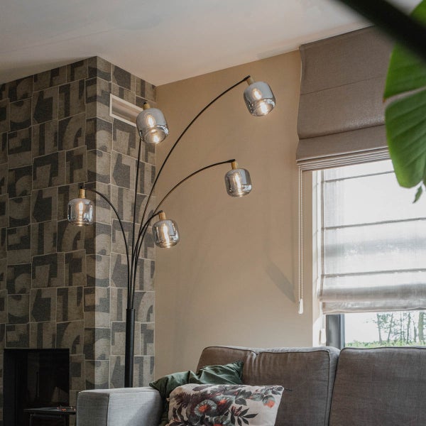 Moderne Bogenstehleuchte mit fünf rauchgrauen Glasschirmen und schwarzem Gestell im Wohnzimmer neben einem grauen Sofa.