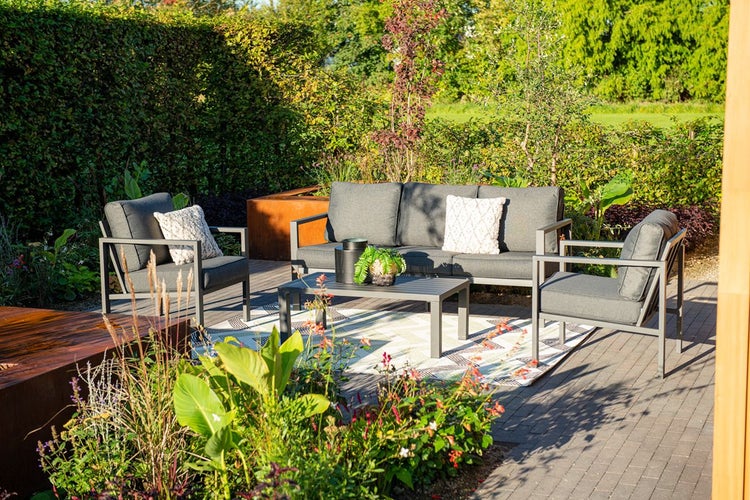 Moderne Garten-Lounge aus Metall mit grauen Polstern, bestehend aus Dreisitzer-Sofa, zwei Sesseln und Tisch in einem hellen, grünen Garten.