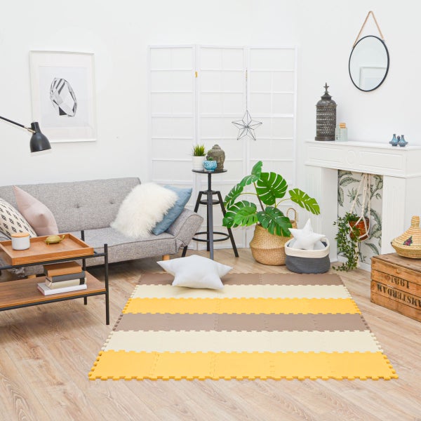 Gestreifte Puzzlematte aus Schaumstoff in einem hellen, organisierten Wohnzimmer mit Sofa, Zimmerpflanzen und Dekoration.