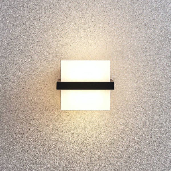 Moderne quadratische LED-Wandleuchte in Schwarz mit weißem satiniertem Schirm, montiert an einer strukturierten Wand mit indirektem Licht.