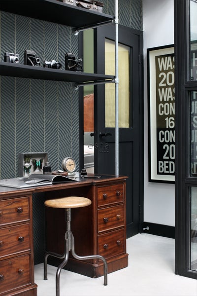 Büro mit Schreibtisch, Stuhl, Regal und dekorativen Vintage-Kameras vor einer gemusterten Tapete