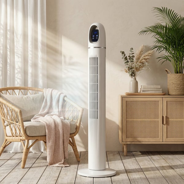 Moderner weißer Turmventilator in einem hellen Wohnzimmer mit Rattan-Sessel, Holz-Sideboard und Zimmerpflanzen.