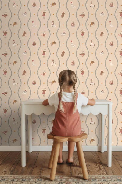 Vliestapete mit Zirkus-Motiven wie Affen und Pferden zwischen Wellenlinien, an einer Wand im Kinderzimmer mit weißem Schreibtisch und Kind.