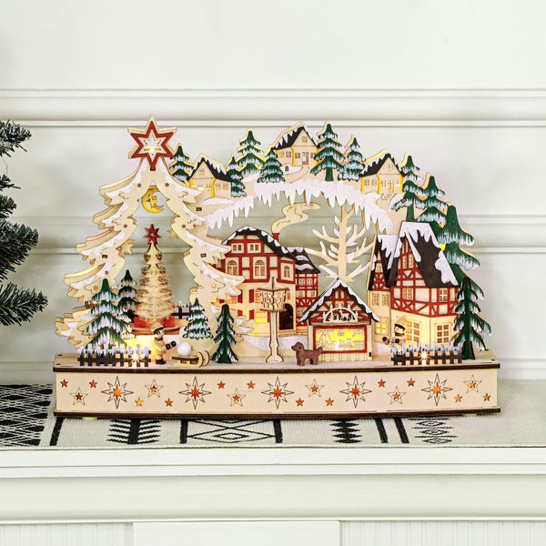 Beleuchtete Weihnachtsdekoration aus Holz mit einer Winterlandschaft, verschneiten Häusern, Tannenbäumen und Figuren.