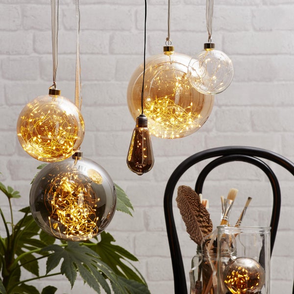 Dekorative Glaskugeln mit LED-Lichterkette und dekorative Glühbirne hängen im Raum.