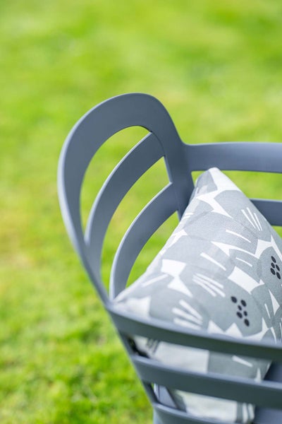 Nahaufnahme eines grauen Gartenstuhls mit gebogener Rückenlehne und einem gemusterten Kissen.