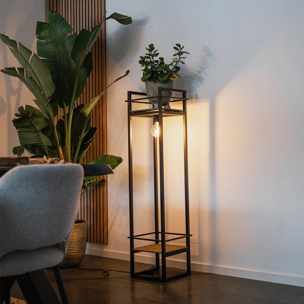 Moderne Stehleuchte aus Metall mit integrierter Ablagefläche für Pflanzen in einem wohnlich eingerichteten Zimmer.