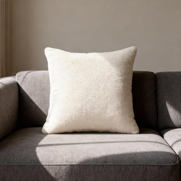 Quadratisches Plüsch-Dekokissen auf einem Sofa.