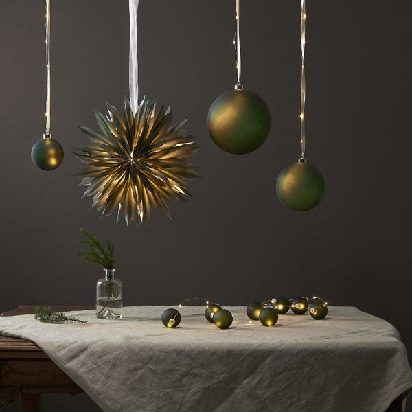 Dekoratives Arrangement mit Weihnachtsstern, Christbaumkugeln und Lichterkette auf einem Tisch