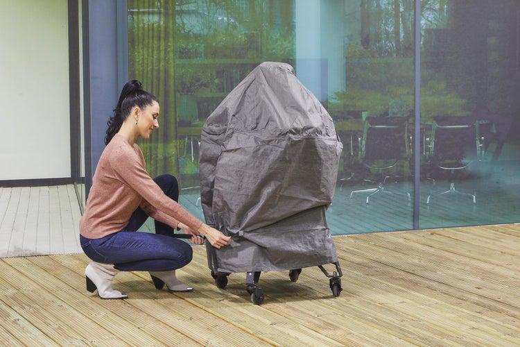 Frau befestigt eine graue Grillabdeckung auf einem Grillwagen